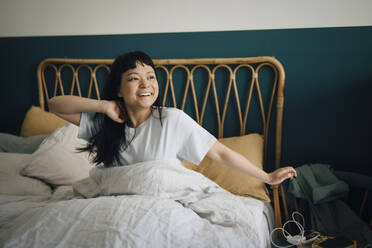 Happy young woman waking up in bed at home - MASF27078