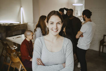 Portrait of confident female professional standing with arms crossed while colleagues in background at office - MASF27099