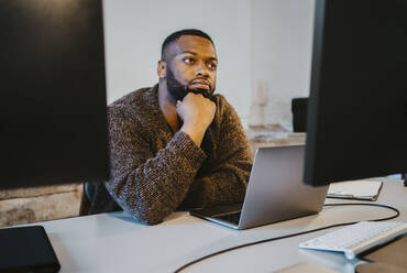 Young male hacker with laptop contemplating in startup company - MASF27124