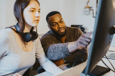 Male hacker discussing with female colleague over computer in startup company - MASF27128