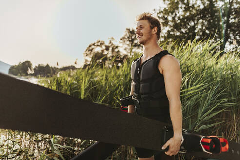 Smiling man wearing life jacket holding waterski - DAWF02078