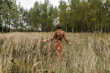 Woman wearing dress walking amidst crops on field - LLUF00267