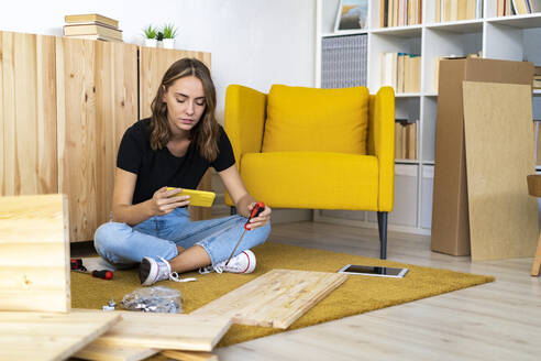 Frau sitzt im Schneidersitz und benutzt ihr Smartphone zu Hause - GIOF13981