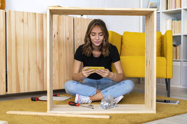 Young woman watching smart phone on carpet - GIOF13986