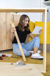 Smiling woman with wood watching digital tablet in living room - GIOF13990