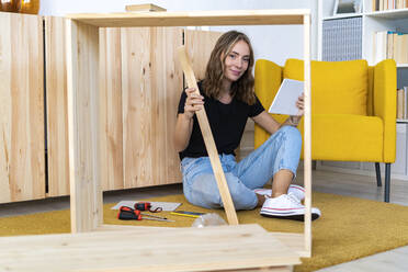Lächelnde junge Frau mit digitalem Tablet und Holz im Wohnzimmer - GIOF13991