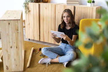 Smiling young woman with digital tablet sitting on ground at home - GIOF13992