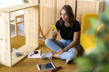 Woman using mobile phone in front of cabinet - GIOF13993