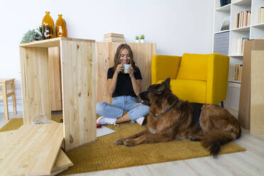 Lächelnde Frau mit Hund beim Kaffee im Wohnzimmer - GIOF13997