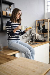 Smiling woman with coffee mug using smart phone on kitchen counter - GIOF14012