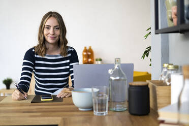 Young woman writing on note pad in kitchen - GIOF14025