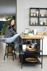 Smiling woman sitting at kitchen counter - GIOF14026
