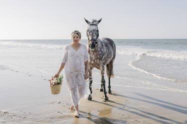 Schwangere Frau mit Pferd bei einem Spaziergang am Strand an einem sonnigen Tag - JRVF02005
