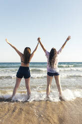 Junge Frauen mit erhobenen Armen, die sich am Strand vergnügen - EGHF00211