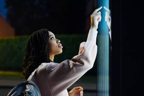 Young woman touching kiosk screen at night - MEUF04704