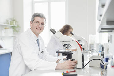 Lächelnde Wissenschaftlerin mit Mikroskop im Labor - AHSF02819