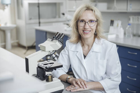 Smiling blond researcher with microscope in laboratory - AHSF02827