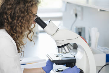 Scientist researching on sample through microscope in laboratory - AHSF02831