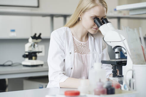 Blonde Wissenschaftlerin, die im Labor durch ein Mikroskop forscht - AHSF02842