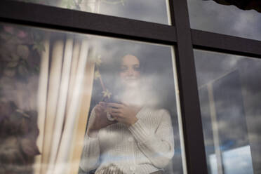 Junge Frau mit Kaffeetasse hinter Fenster - LLUF00280