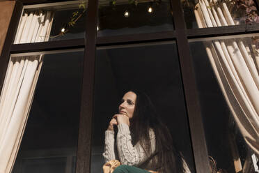 Woman with hand on chin looking out of window - LLUF00285