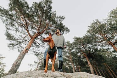 Smiling woman and dog looking away on rock - MRRF01641