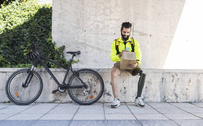 Disabled delivery man scanning box with smart phone in public park - JCCMF04344