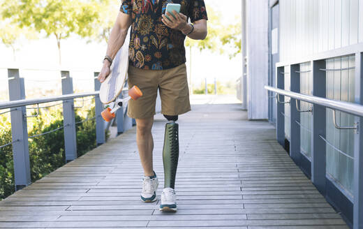 Mann mit Beinprothese benutzt Handy auf der Strandpromenade - JCCMF04347