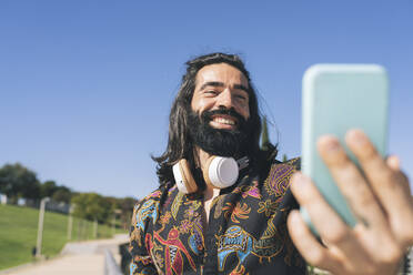 Glücklicher bärtiger Mann nimmt Selfie durch Smartphone im Park - JCCMF04352