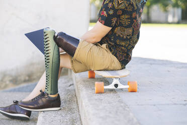 Man with prosthetic leg using laptop on steps - JCCMF04355