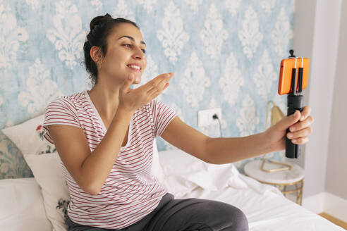 Lächelnde Influencerin, die im Schlafzimmer einen Vlog über ihr Mobiltelefon führt - JRVF02022