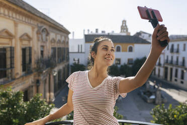 Lächelnde Influencerin, die auf einem Balkon mit dem Handy filmt - JRVF02023