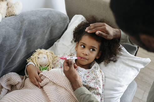 Besorgter Vater, der das Fieber seiner Tochter mit Hilfe eines Thermometers auf dem Sofa kontrolliert - VYF00600