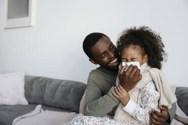 Glücklicher Vater mit Taschentuch wischt seiner Tochter zu Hause die Nase ab - VYF00610