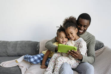 Smiling man with son and daughter using digital tablet on sofa - VYF00614