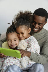 Smiling man with daughter and son watching digital tablet at home - VYF00617