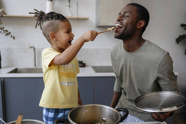 Boy feeding spaghetti to father in kitchen - VYF00623