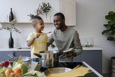 Lächelnder Junge zeigt dem Vater in der Küche Spaghetti - VYF00625