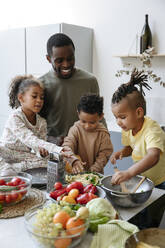 Brüder und Schwester bereiten mit dem Vater in der Küche Essen zu - VYF00629