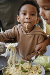 Süßer Junge isst Spaghetti inmitten von Bruder und Vater in der Küche - VYF00637