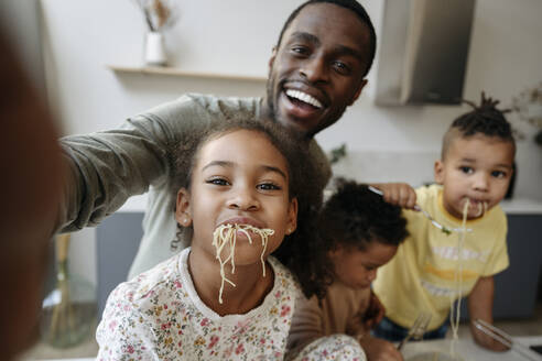 Glücklicher Mann, der ein Selfie mit Tochter und Söhnen macht, die in der Küche Spaghetti essen - VYF00641