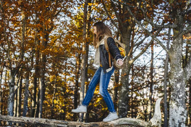Junge Frau balanciert auf einem Baumstamm im Herbstwald - MCVF00930
