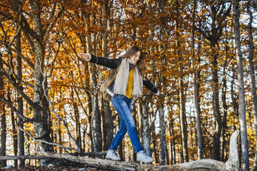 Smiling woman with arms outstretched balancing on tree trunk - MCVF00931