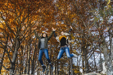 Carefree friends jumping in autumn forest - MCVF00932
