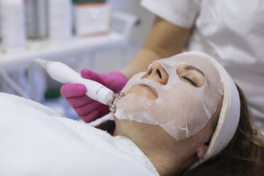 Woman with sheet mask getting beauty treatment in salon - MOMF00941