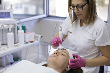 Kosmetikerin bei der Ultraschall-Gesichtsbehandlung einer reifen Frau mit Geräten im Salon - MOMF00945