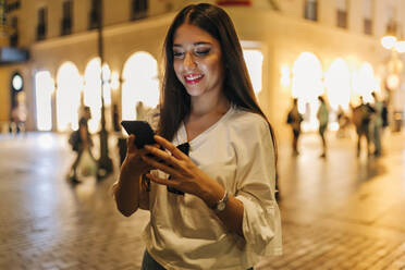 Smiling woman using smart phone at street in city - JRVF02036