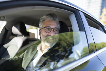 Smiling businessman with eyeglasses driving car - JCCMF04372