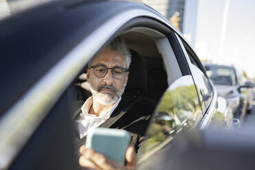 Businessman looking at smart phone in car - JCCMF04374