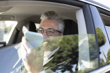 Businessman talking on smart phone in car - JCCMF04375